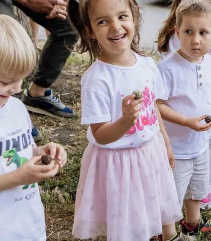 Nasmejana devojčica sa kikicama i roze tutu suknjicom drži grudvicu zemlje