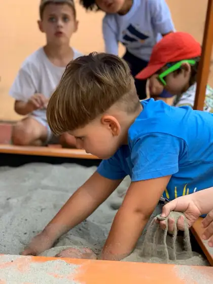 Dečak u plavoj majici klečeći nad peskarom propušta pesak kroz prste