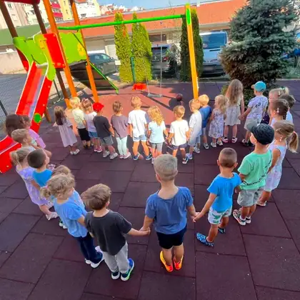Cela grupa dece drži se za ruke u velikom krugu na dvorišnom igralištu sa mekom gumenom podlogom