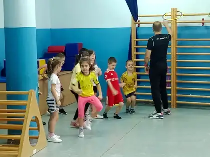 Čas sporta u fiskulturnoj sali: deca u šarenim dresovima trče u koloni