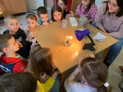 Deca sede oko stola i pažljivo posmatraju ogled o kruženju vode u prirodi: stona lampa greje staklenu posudu sa vodom