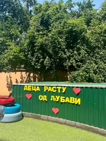 Natpis „Deca rastu od ljubavi” sa crvenim srcima na zelenoj ogradi dvorišta