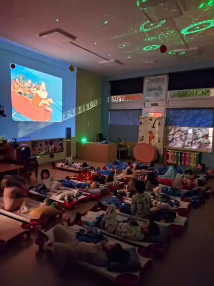 Deca leže na dušecima u zamračenoj sobi i gledaju crtani film na platnu