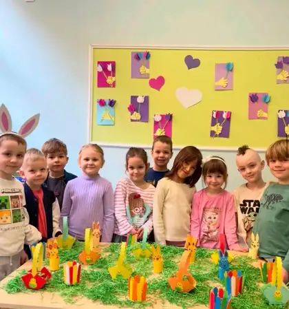 Deca poziraju iza stola sa uskršnjim zečevima koje su napravila, a na zidu iza njih su srca i dečiji radovi